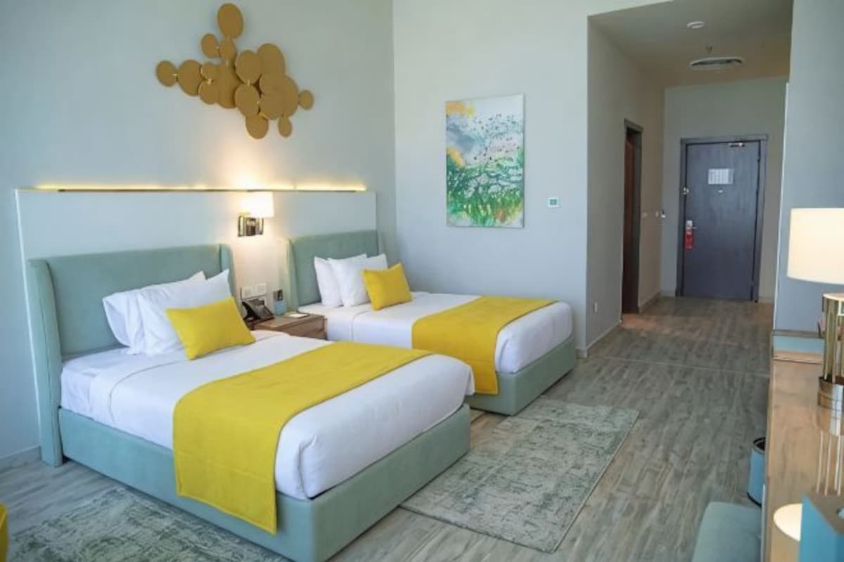 Une chambre d’hôtel avec deux lits, une table de chevet, une lampe, un tableau et une porte.