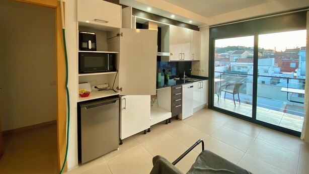 A modern kitchen with white cabinets, a built-in microwave, and a dishwasher. There is a large window providing a view of the cityscape.