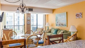 A cozy living area with a dining table, wicker chairs, a green sofa, and a painting on the wall. - Oceanfront Building With Great Ocean and Bay Views (Ocean City)