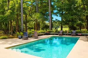 Una piscina rectangular con agua cristalina azul, rodeada de abundante vegetación y árboles, con sillas de descanso y un cartel que dice 'NO DIVING'.