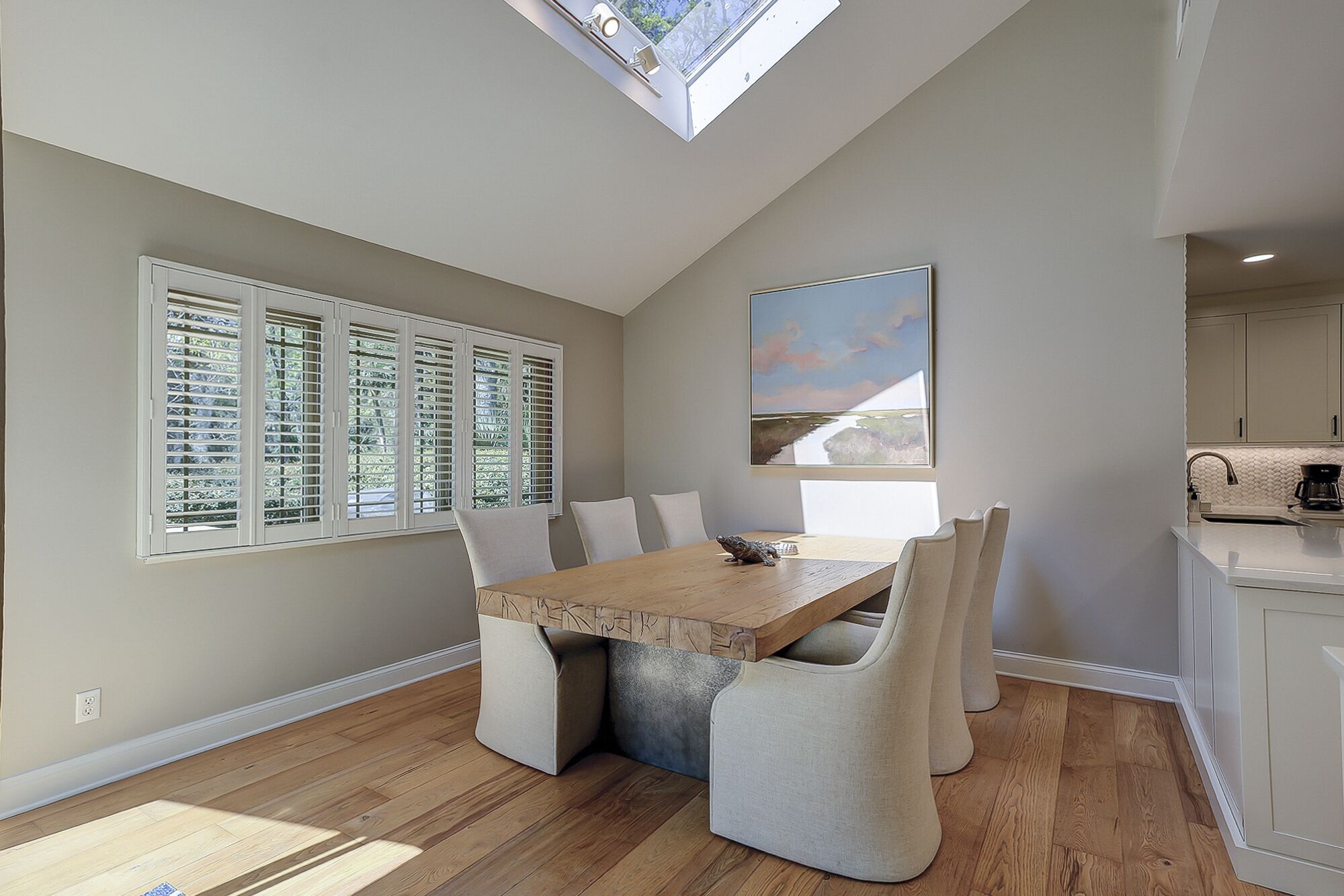 A dining area with a wooden table and chairs, a skylight, and a painting on the wall.