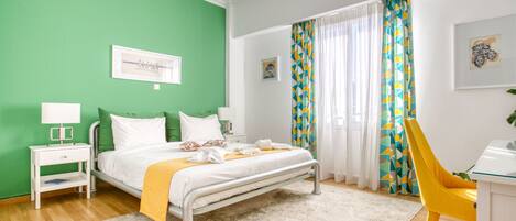Quarto de hotel com cama, mesa de cabeceira, cadeira e janela com cortinas.