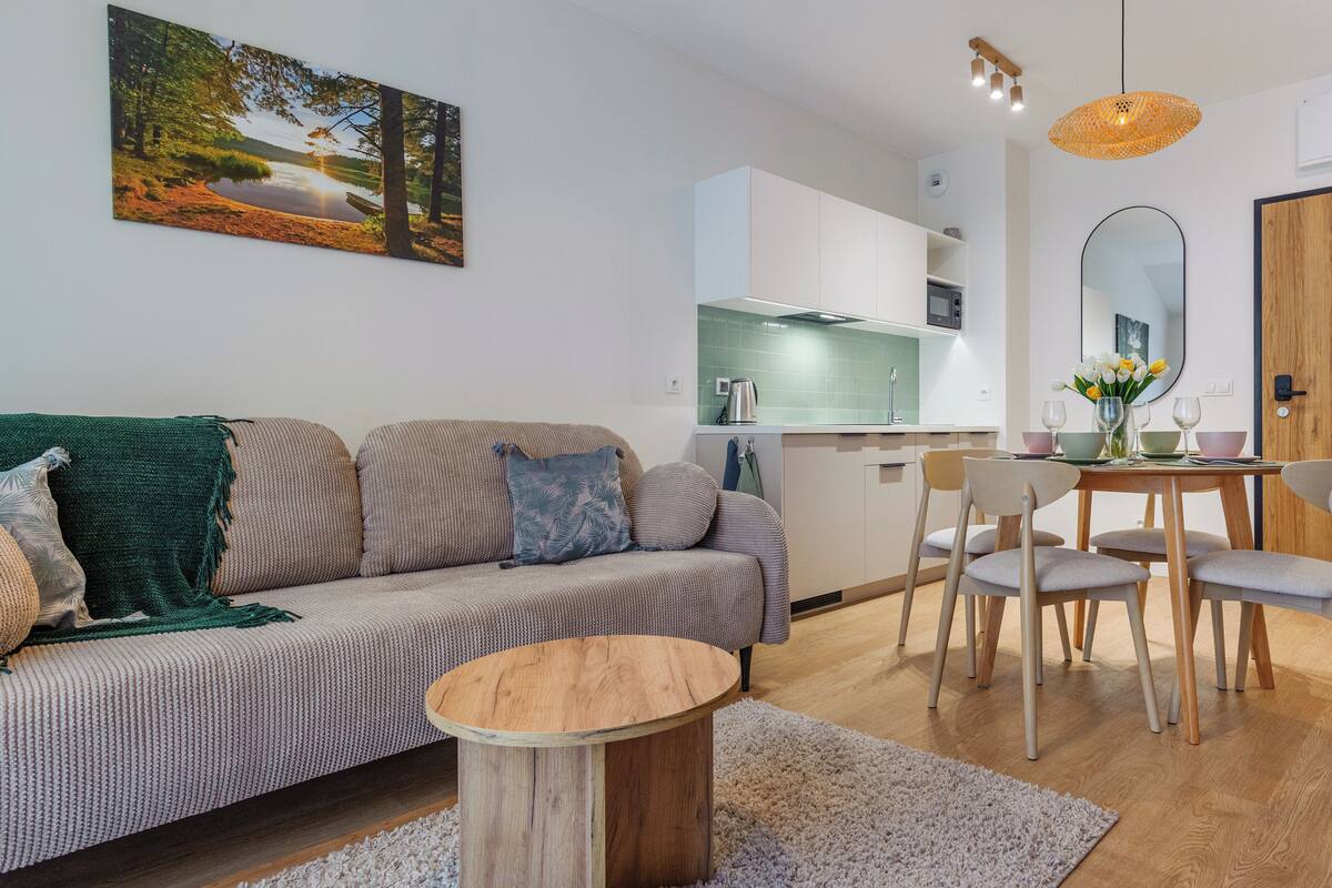 Una sala de estar moderna con un sofá, una mesa de centro redonda de madera y un comedor con mesa y sillas.