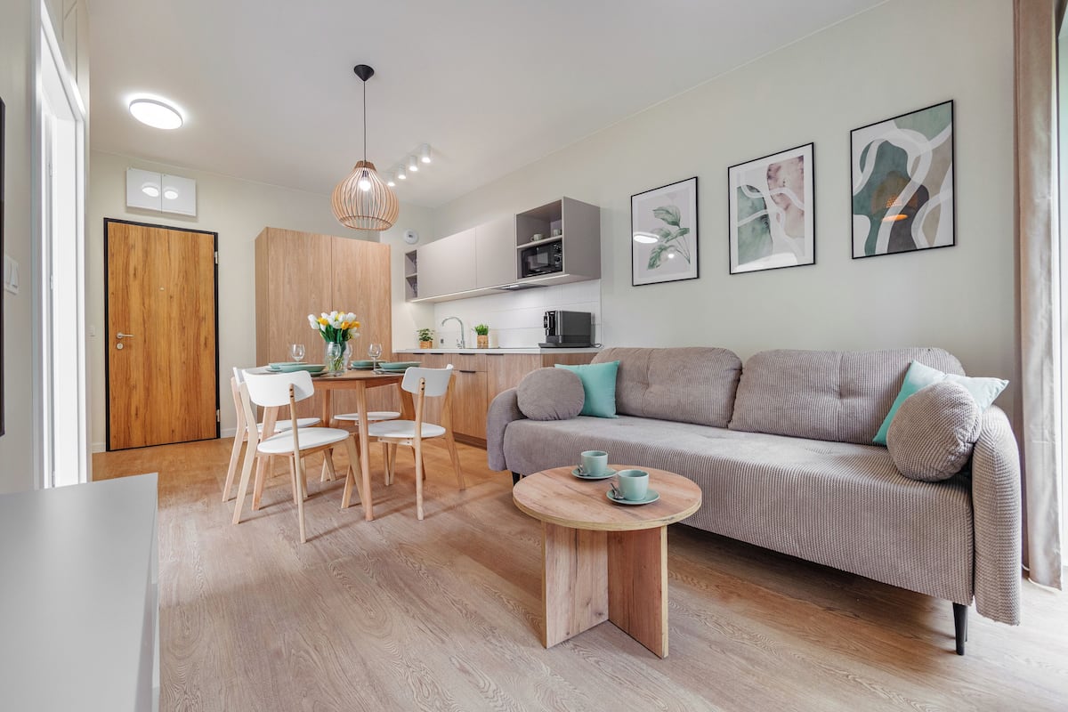 Una sala de estar moderna con un sofá, una mesa de comedor con sillas, una mesa de centro y una zona de cocina al fondo.