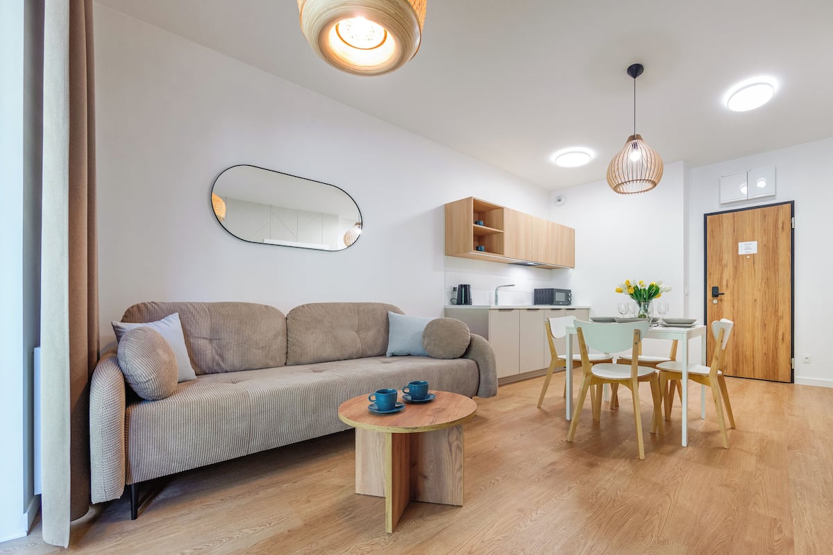 Una sala de estar moderna con un sofá, una mesa de comedor con sillas, una zona de cocina y una puerta de madera.