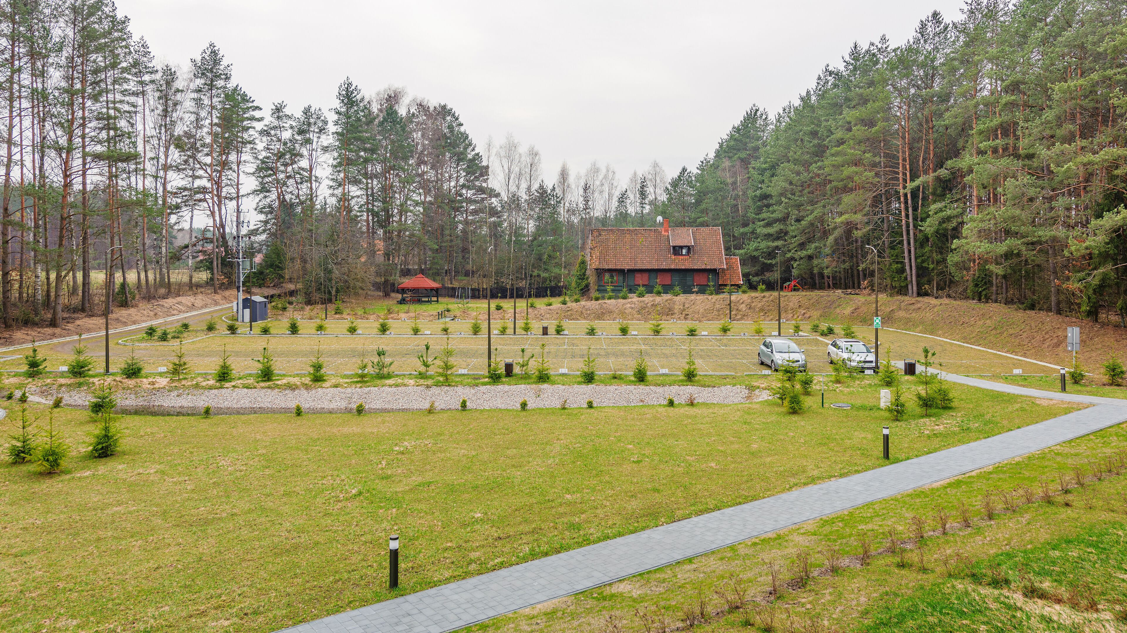 A parking lot with a paved walkway, surrounded by trees and a building with a red roof.