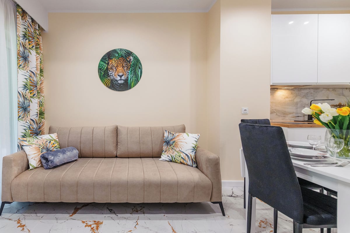 Una sala de estar con un sofá, una mesa de comedor con sillas, una zona de cocina y un cuadro decorativo en la pared.