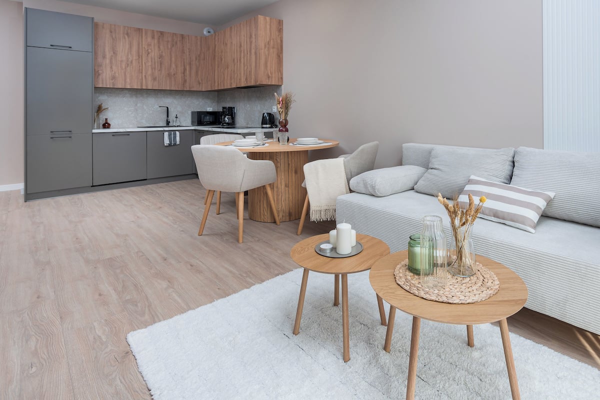 Una sala moderna con un sofá gris, una mesa de comedor de madera y una cocina al fondo.