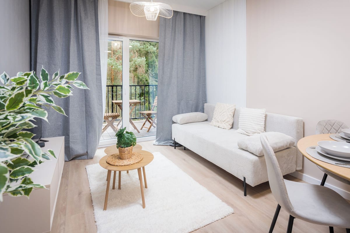 Una sala de estar moderna con un sofá, una mesa de comedor y un balcón con mobiliario exterior.