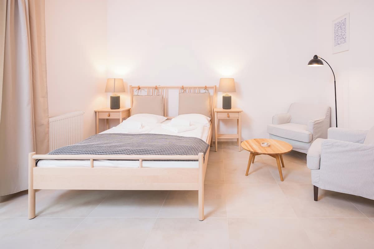 Un dormitorio con cama, mesitas de noche, una silla, una lámpara y una pequeña mesa.