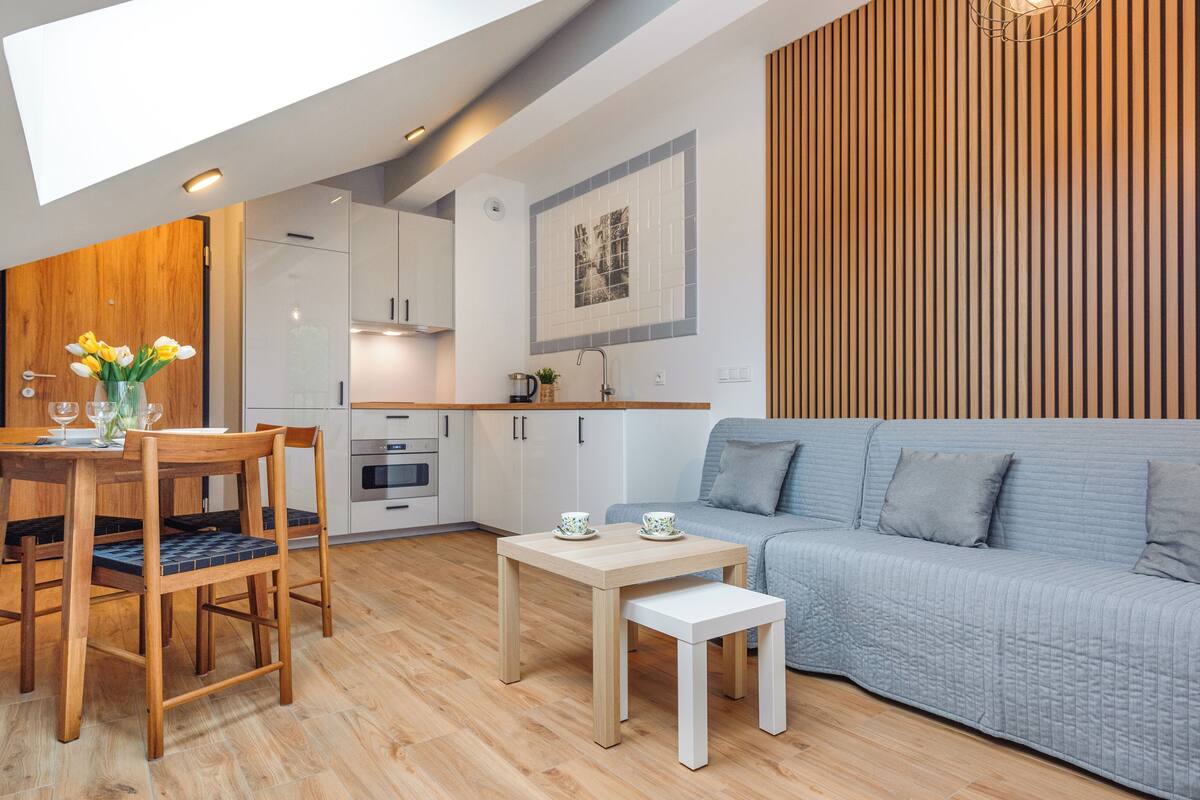 Una cocina moderna con armarios blancos, una mesa de comedor de madera con sillas, un sofá gris y una mesita auxiliar blanca.