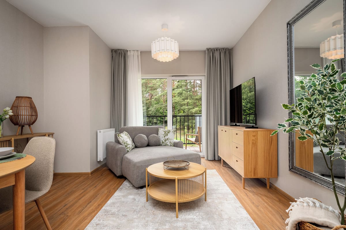 Una sala moderna con sofá, televisión, mueble de madera y comedor con mesa y sillas.