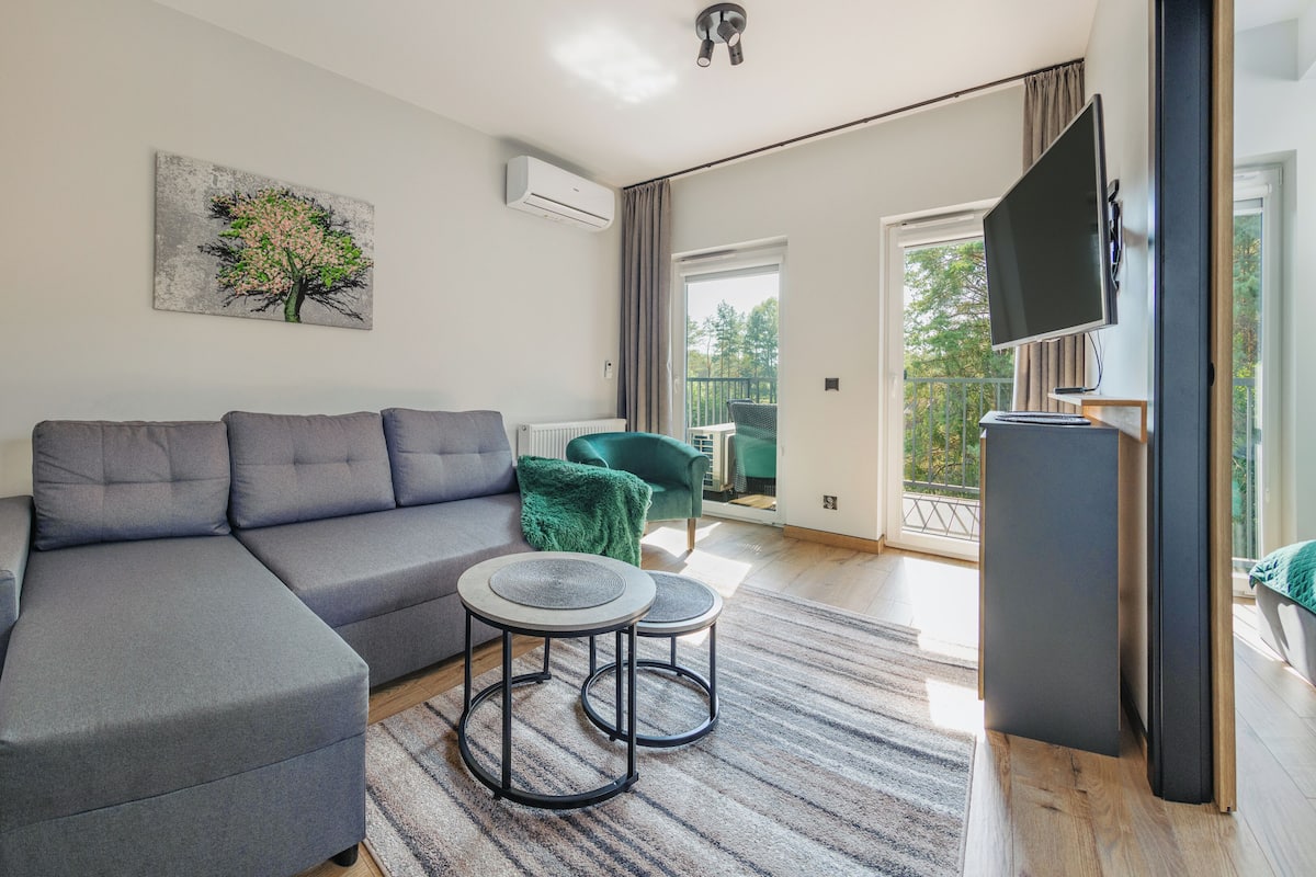 Una sala de estar moderna con un sofá seccional gris, una mesa de centro redonda, un sillón verde y un cuadro de un árbol.