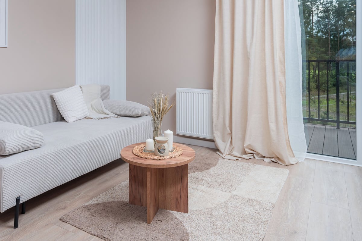 Una sala de estar moderna con un sofá, una mesita redonda de madera y vistas a través de un gran ventanal.
