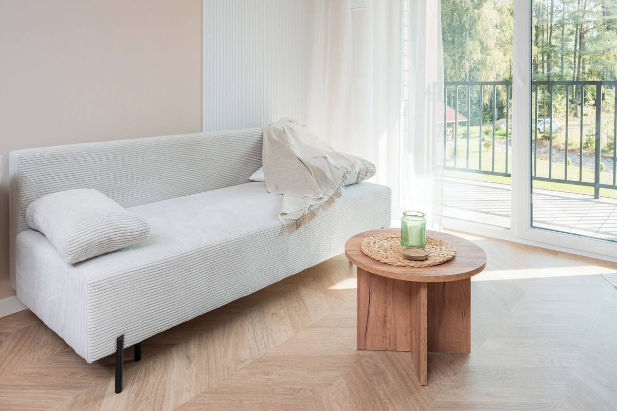 Una sala de estar moderna con un sofá, una mesa de centro redonda de madera y vistas a un balcón.