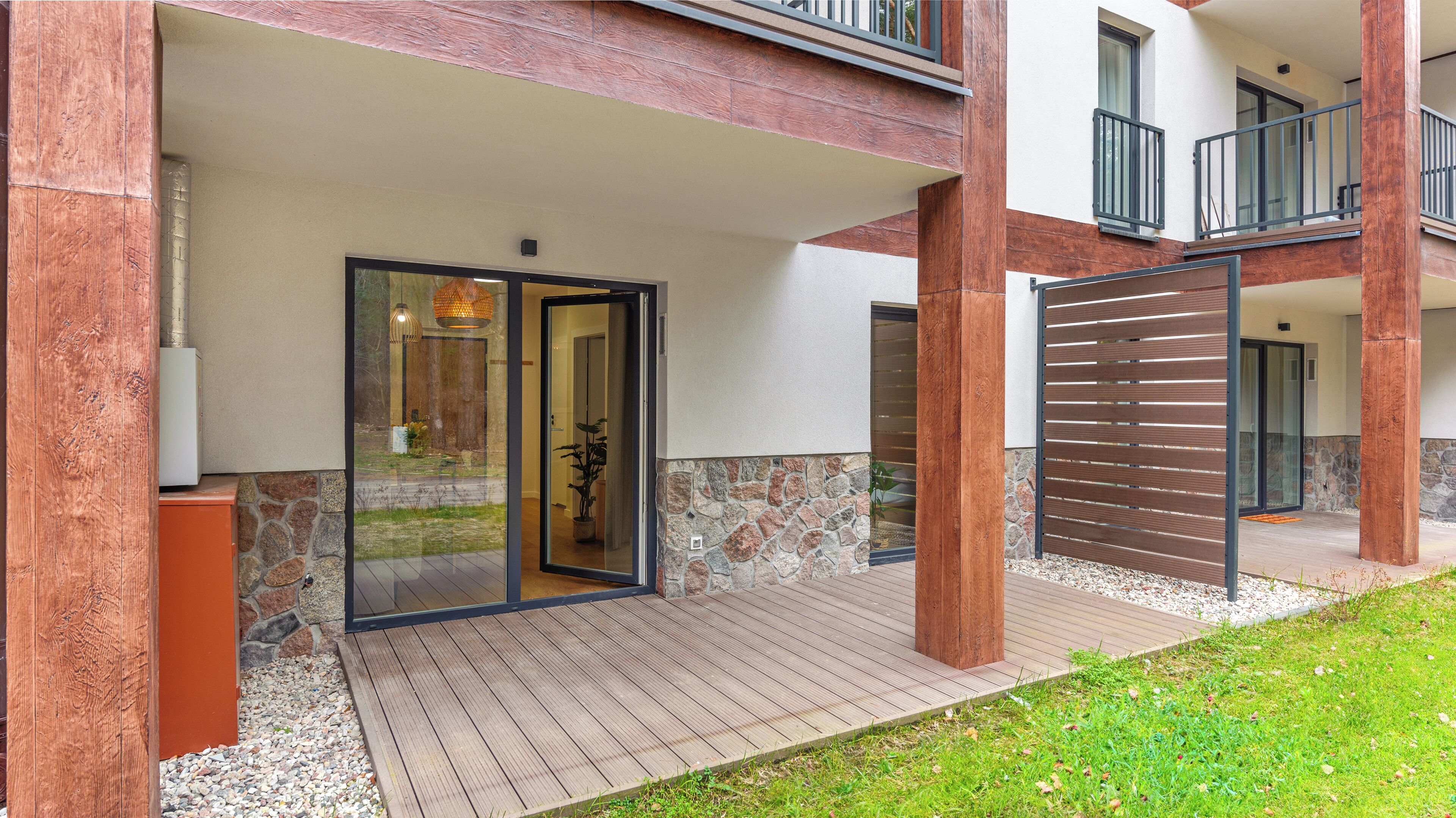 A modern building with a covered entrance, stone wall, and wooden deck.