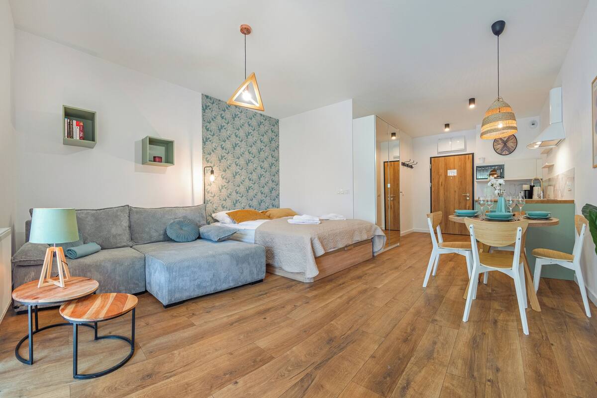 Una sala de estar moderna con sofá, mesa de comedor con sillas, área de cocina y un ventanal grande.