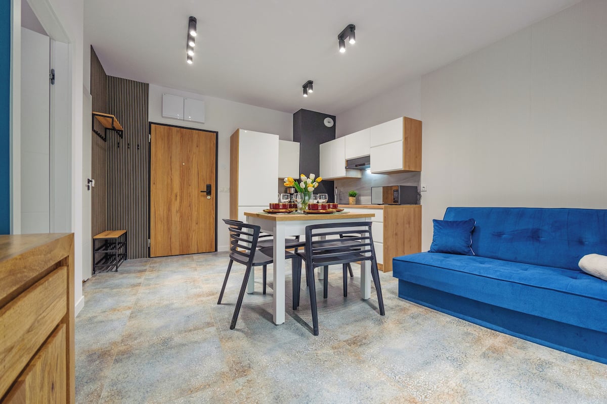 Una cocina moderna con armarios blancos, un sofá azul y una zona de comedor con sillas y una mesa.