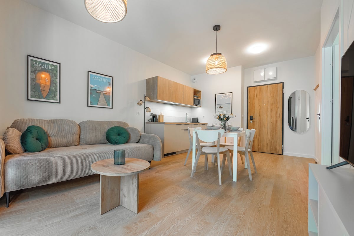 Una sala de estar moderna con un sofá, una mesa de comedor con sillas, una zona de cocina y una puerta de madera.