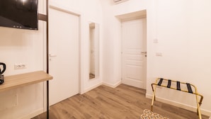Una habitación con una televisión de pantalla plana montada en la pared, piso de madera y un pequeño banco con cojín a rayas.