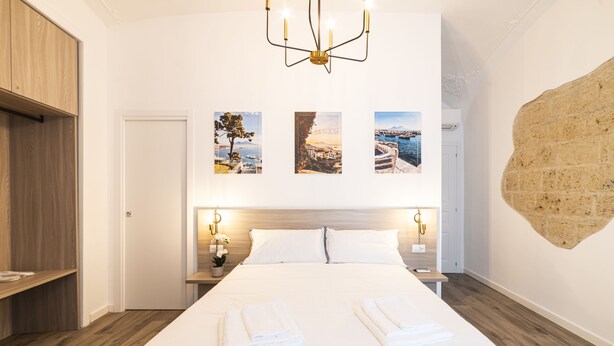 Habitación de hotel con una cama grande, suelo de madera, un candelabro y tres cuadros en la pared.