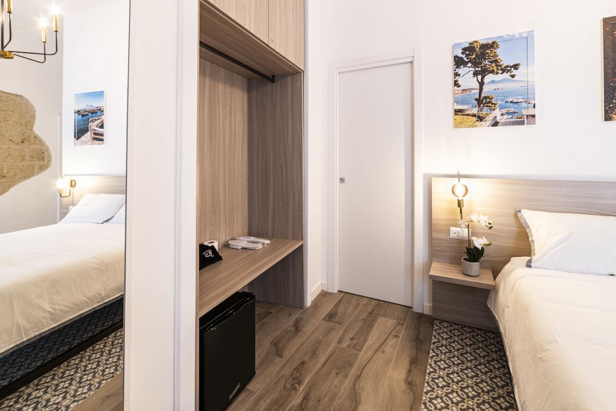 Habitación de hotel con cama, escritorio y armario. Hay una mesita con lámpara y planta en maceta.