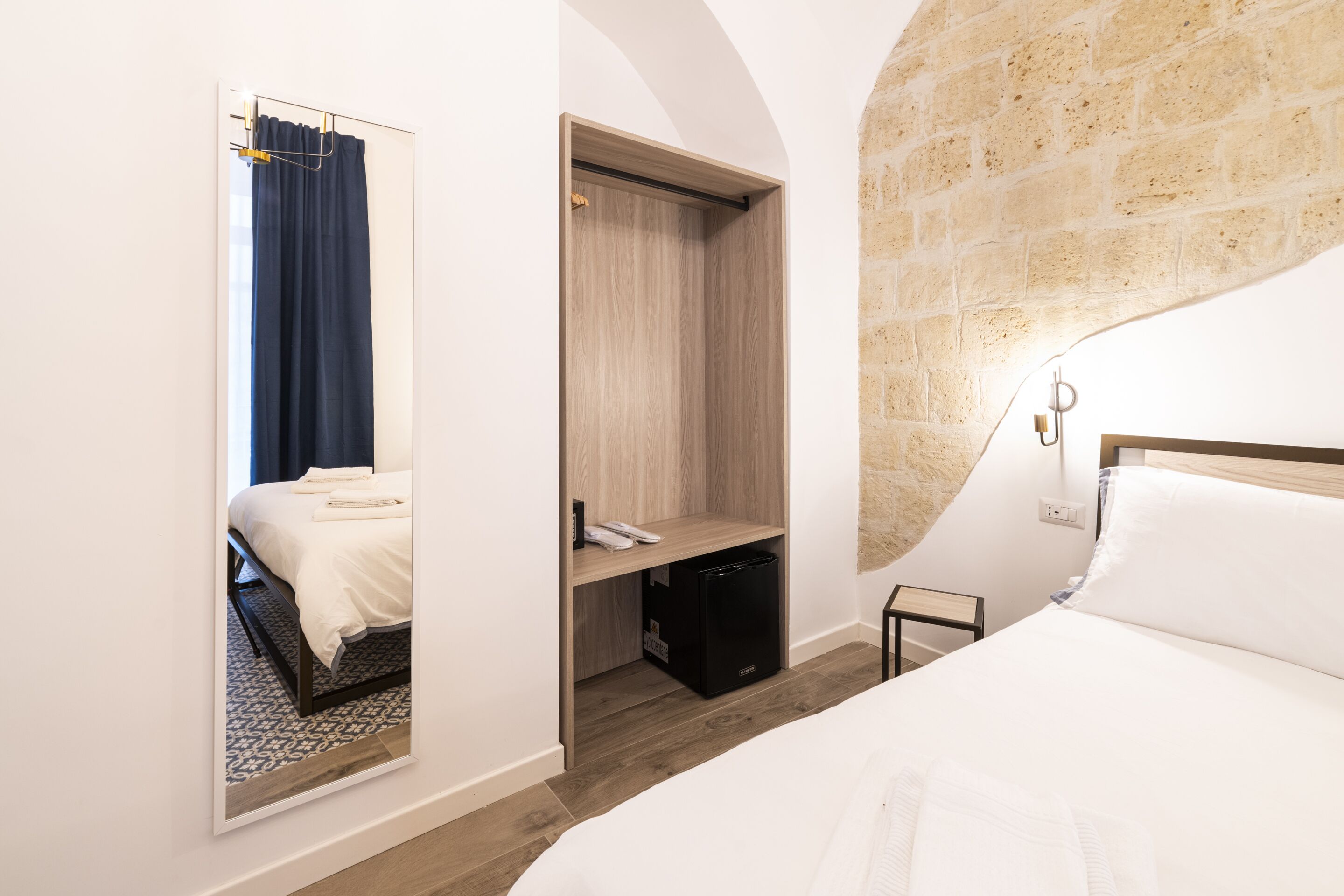Une chambre d’hôtel avec un lit, une armoire, un miroir et une petite table de chevet.