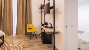 Habitación de hotel moderna con un escritorio de madera, una silla amarilla, un televisor de pantalla plana montado sobre un soporte de metal negro y un refrigerador pequeño negro.
