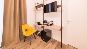 Una habitación compacta con escritorio, silla, televisión, cafetera y un refrigerador pequeño.