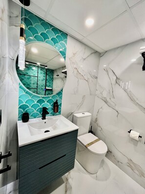 Une salle de bain avec un lavabo blanc, un miroir, des toilettes et un mur orné d’un motif turquoise.