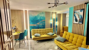 A modern living room with a yellow sofa, a dining area with a table and chairs, and a large abstract mural on the wall. - TresColores  (Alicante)