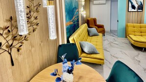 A modern living room with a yellow sofa, a green chair, and a wooden dining table with a vase of flowers. - TresColores  (Alicante)