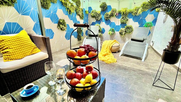 A sunlit outdoor seating area with a wicker sofa, a table with a fruit basket, and a potted plant. - TresColores  (Alicante)