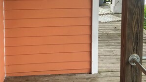 Una terraza de madera con barandilla, una puerta con pomo de latón y una pared con dos ventanas circulares.