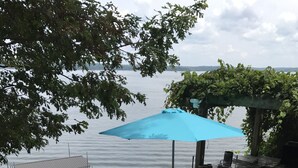 Un patio con vistas al agua, una fogata, mobiliario exterior y una zona de parrilla techada.