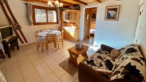 Ein gemütliches Wohnzimmer mit Holzboden, eine Essecke mit Tisch und Stühlen, eine Küche mit Holzschränken und ein Sofa mit Kuhfellbezug.