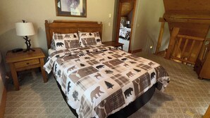 A bedroom with a bed, a nightstand, a lamp, a framed picture on the wall, and a wooden chair.