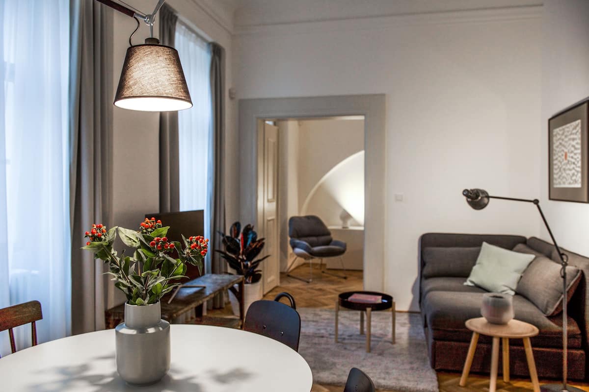A modern living room with a round table, a sofa, and a chair. There is a vase with flowers on the table.