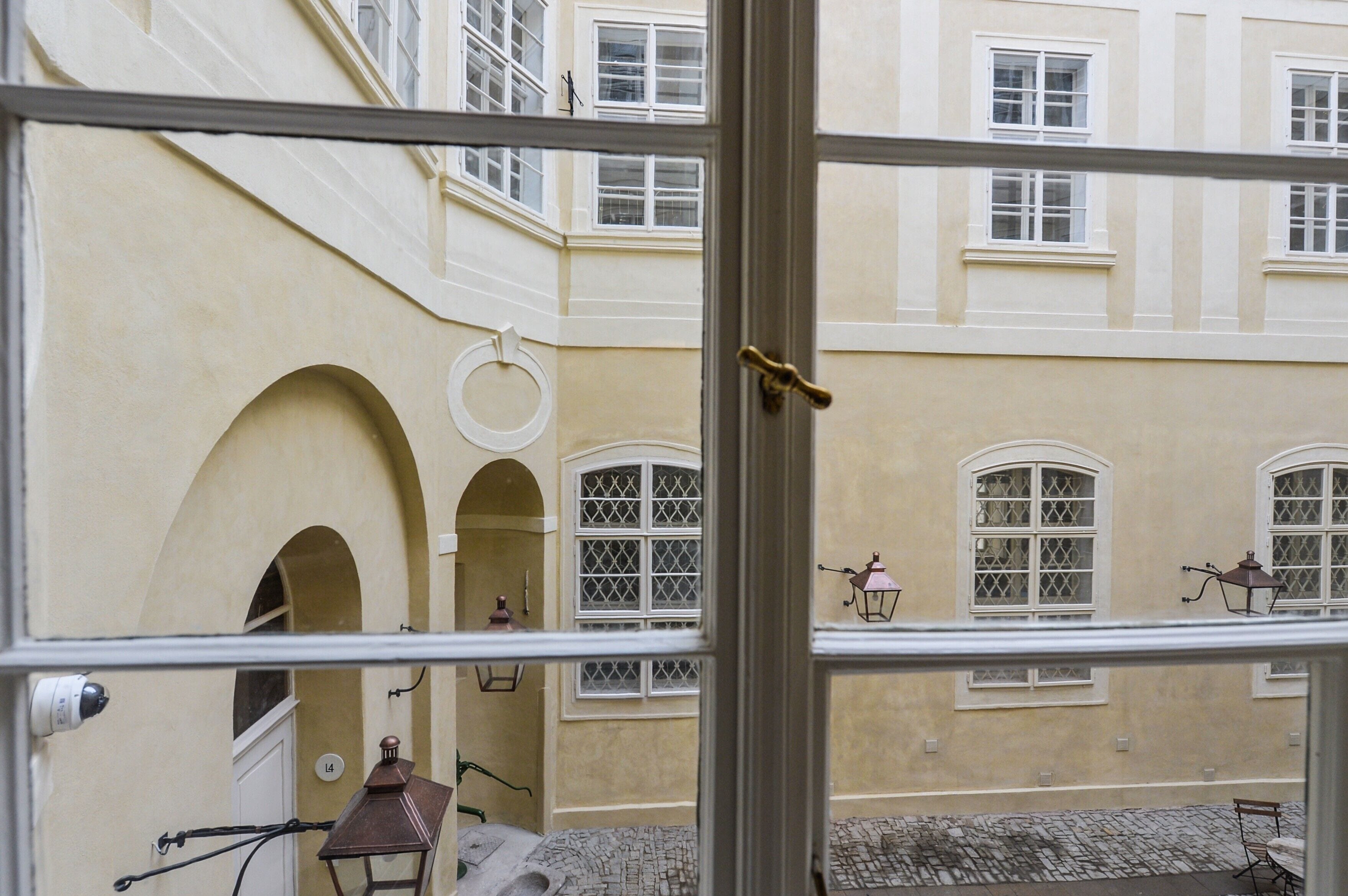 A courtyard with arched doorways, a cobblestone path, and a building with multiple windows and a lantern.