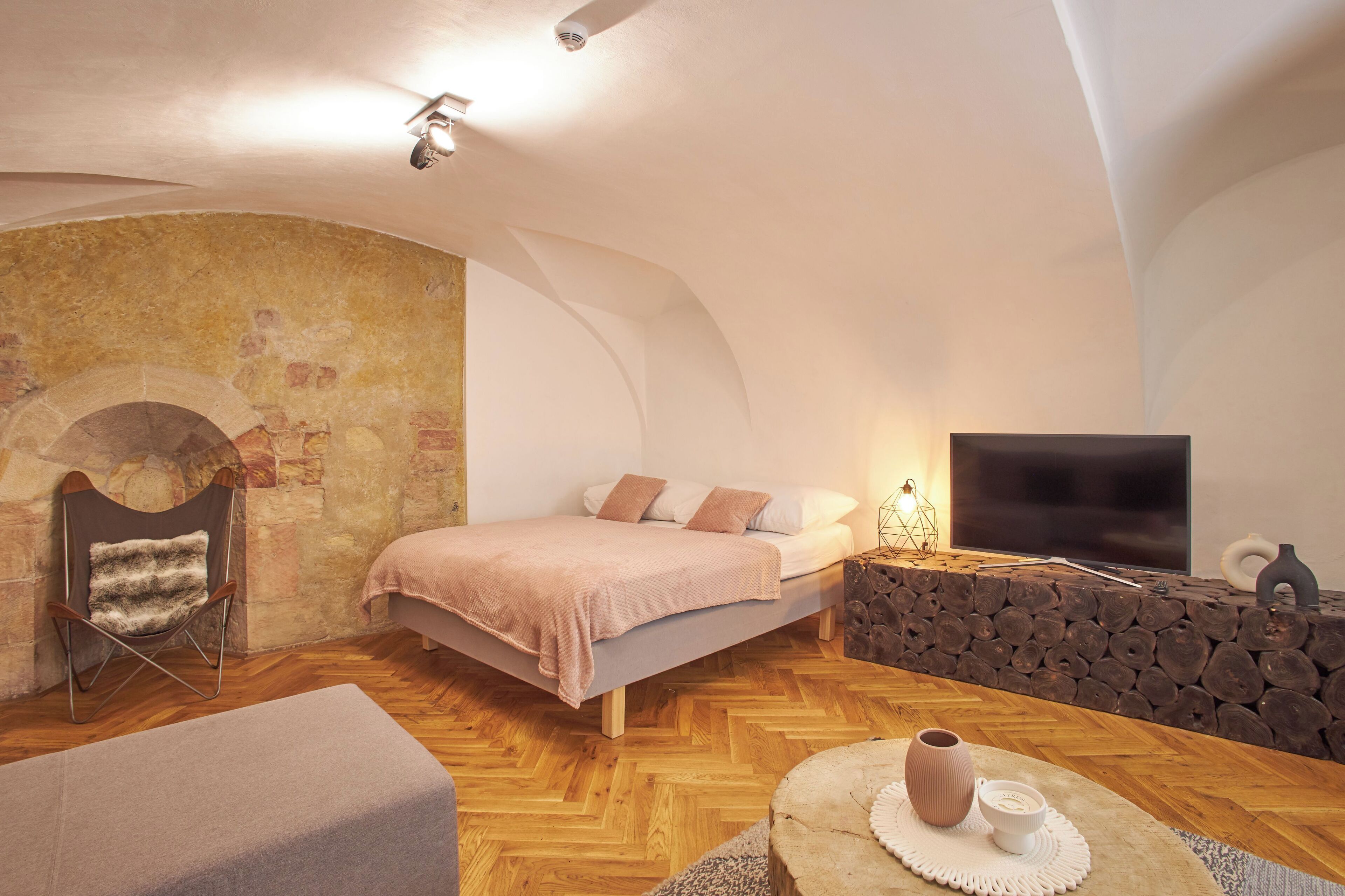 Une chambre confortable avec un mur en pierre, un lit recouvert d’une couverture rose, une télévision et une cheminée.