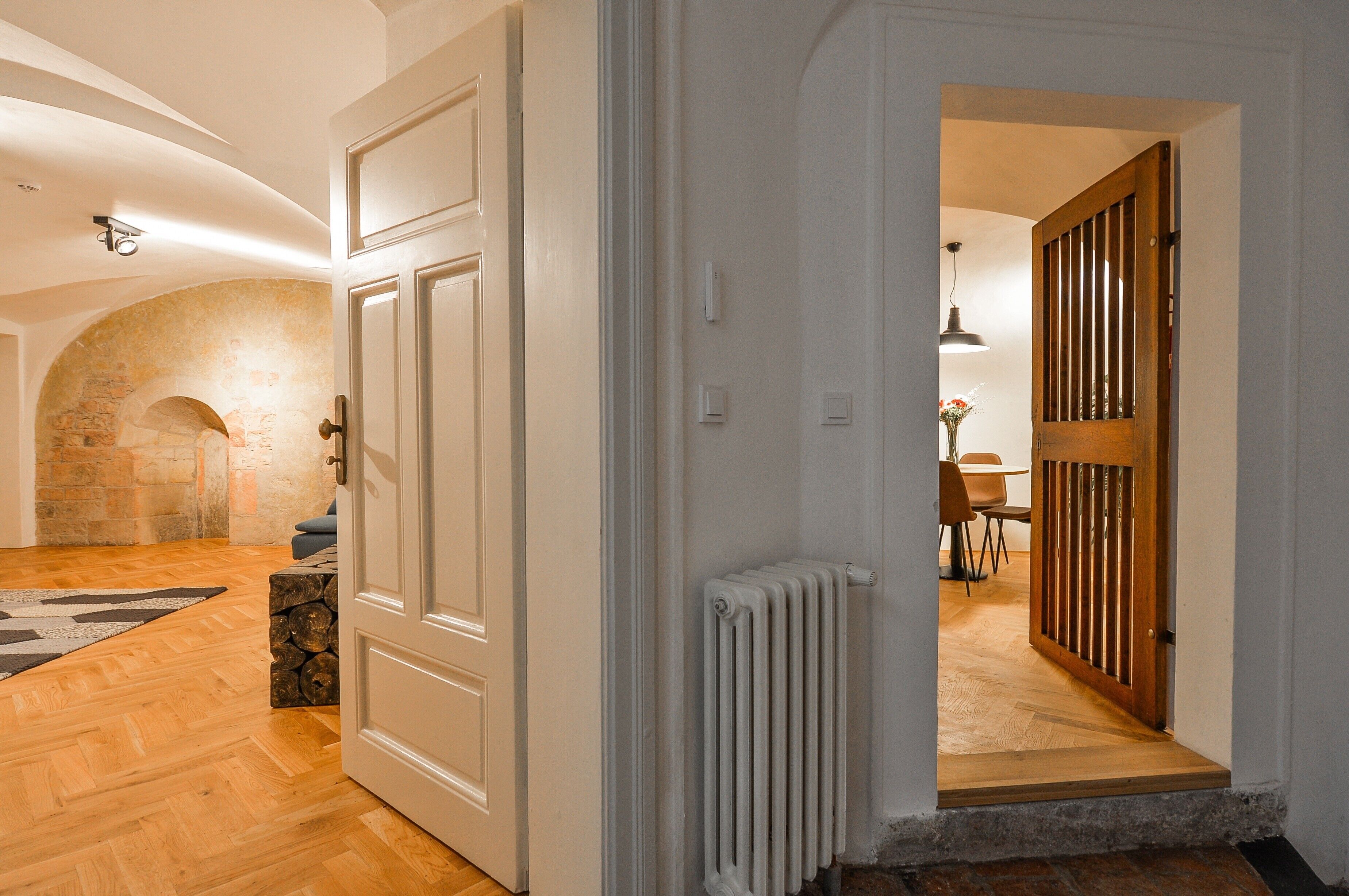 Un couloir avec un plancher en bois, des portes blanches, un radiateur et un mur en pierre.
