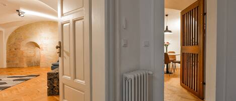 Un couloir avec un plancher en bois, des portes blanches, un radiateur et un mur en pierre.