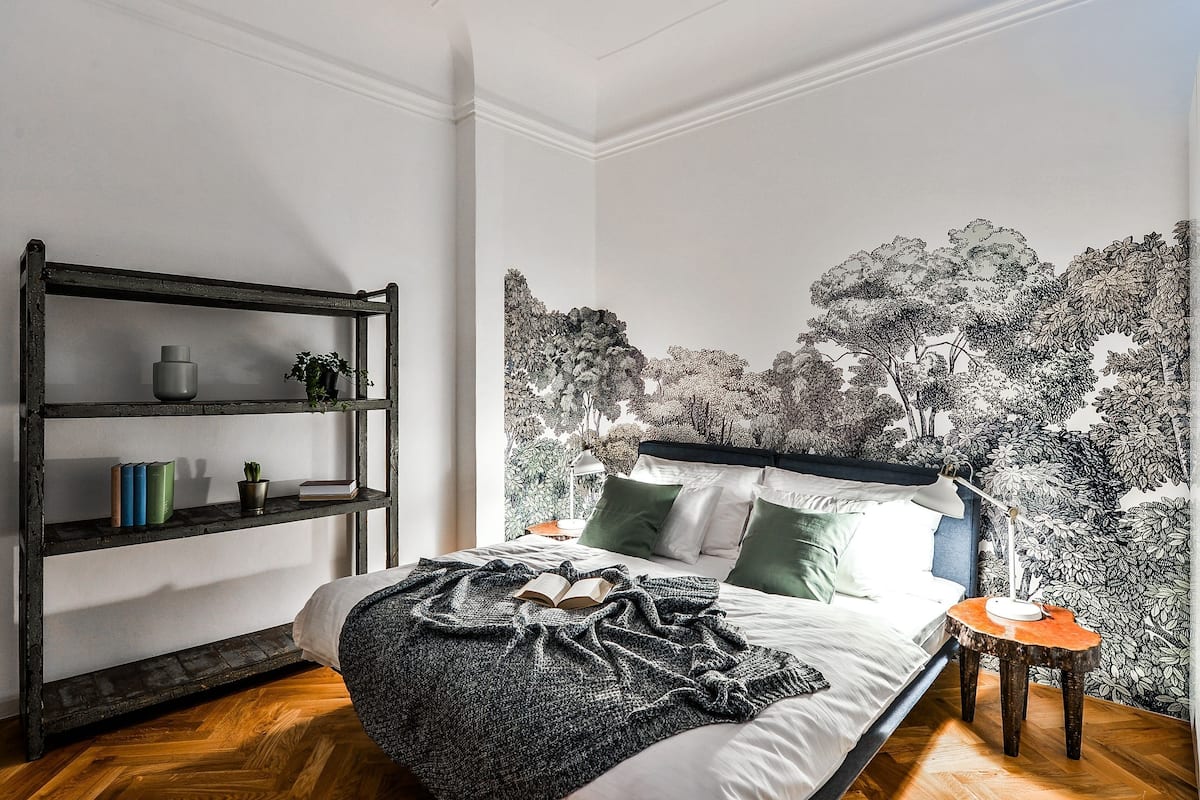 A bedroom with a bed, a bookshelf, a wall mural, and a nightstand.