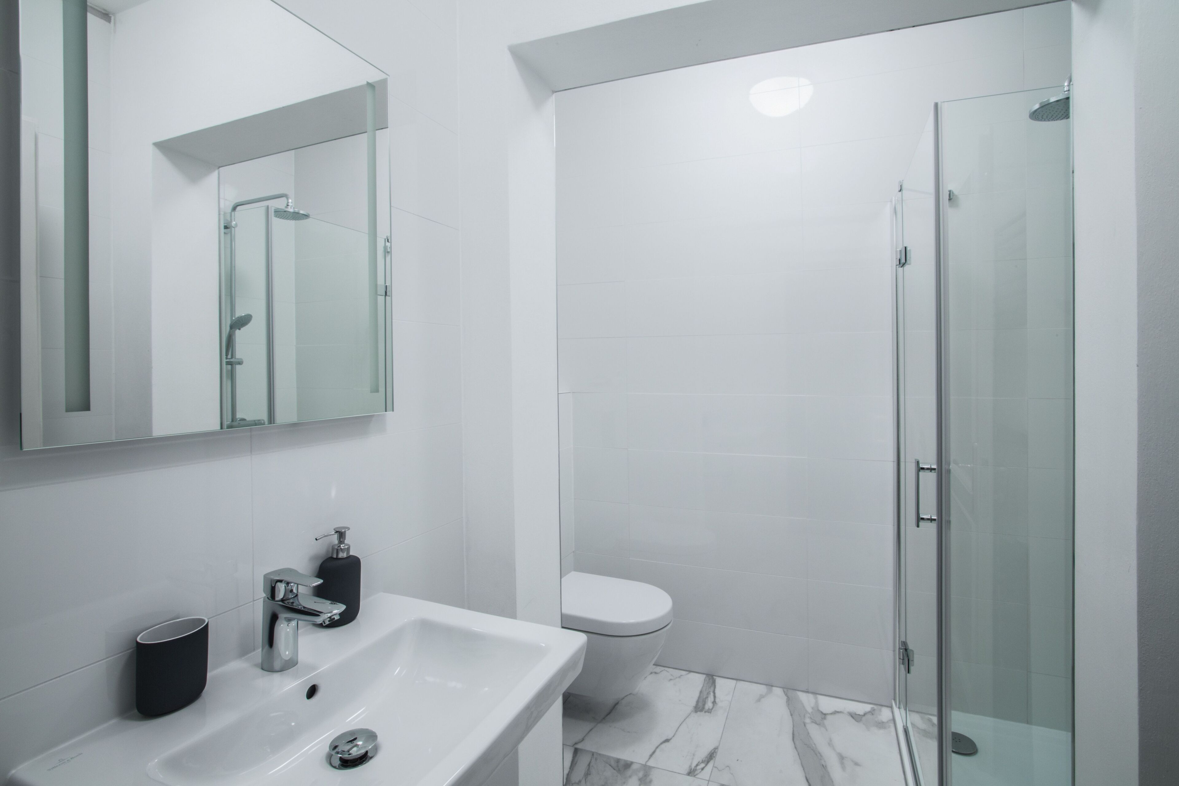 A modern bathroom with a white sink, a mirror, a glass shower enclosure, and a toilet.