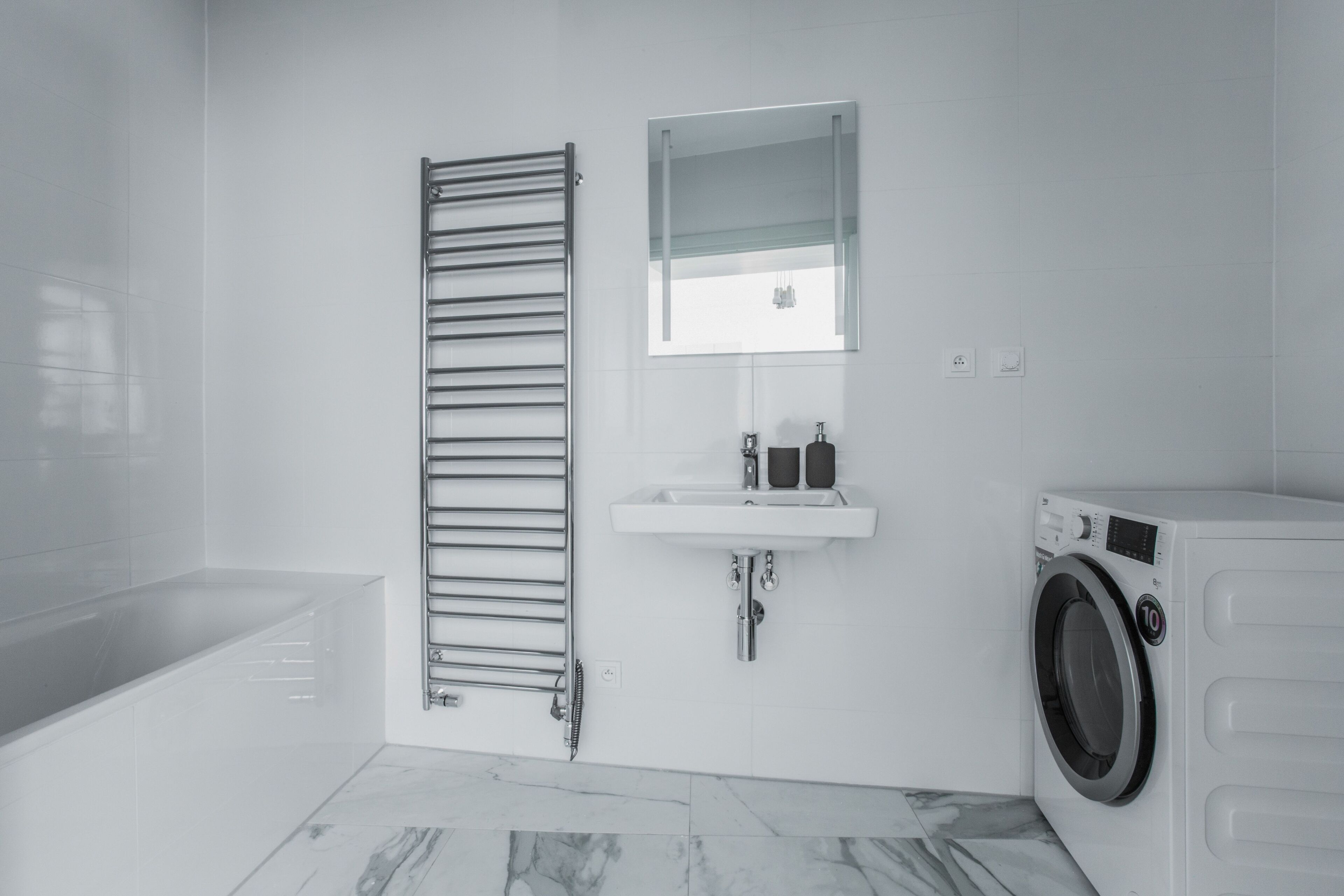 A modern bathroom with a bathtub, a towel rack, a sink, and a washing machine.