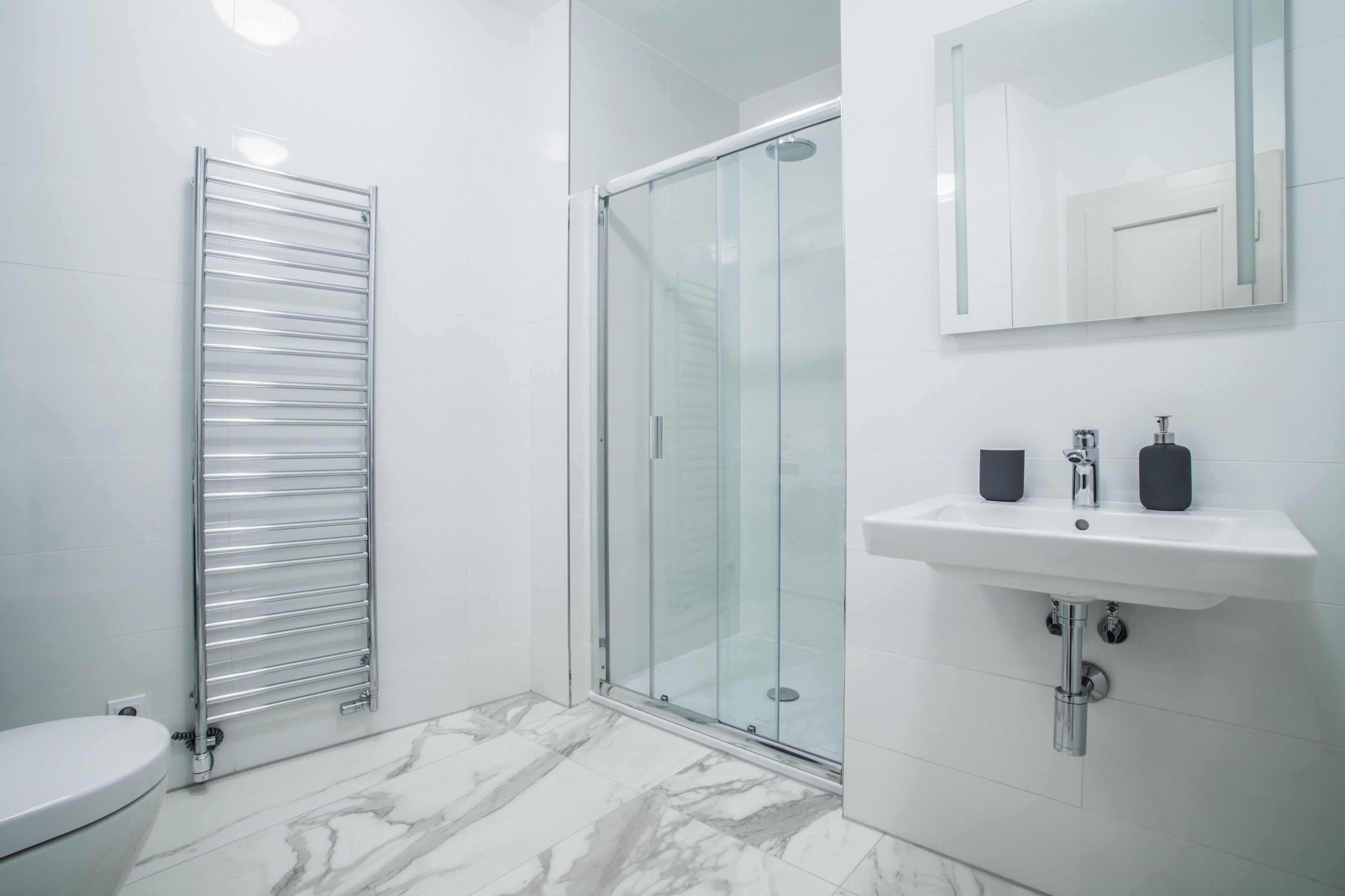 A modern bathroom with a glass shower enclosure, a white sink with two soap dispensers, and a towel rack.