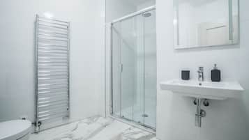 A modern bathroom with a glass shower enclosure, a white sink with two soap dispensers, and a towel rack.