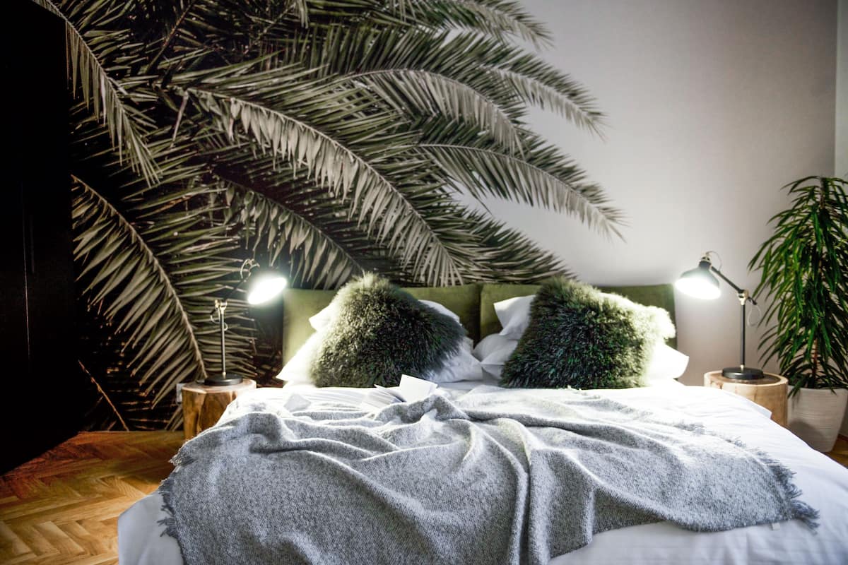 A bed with a white comforter, two green pillows, and a large palm tree in the background.