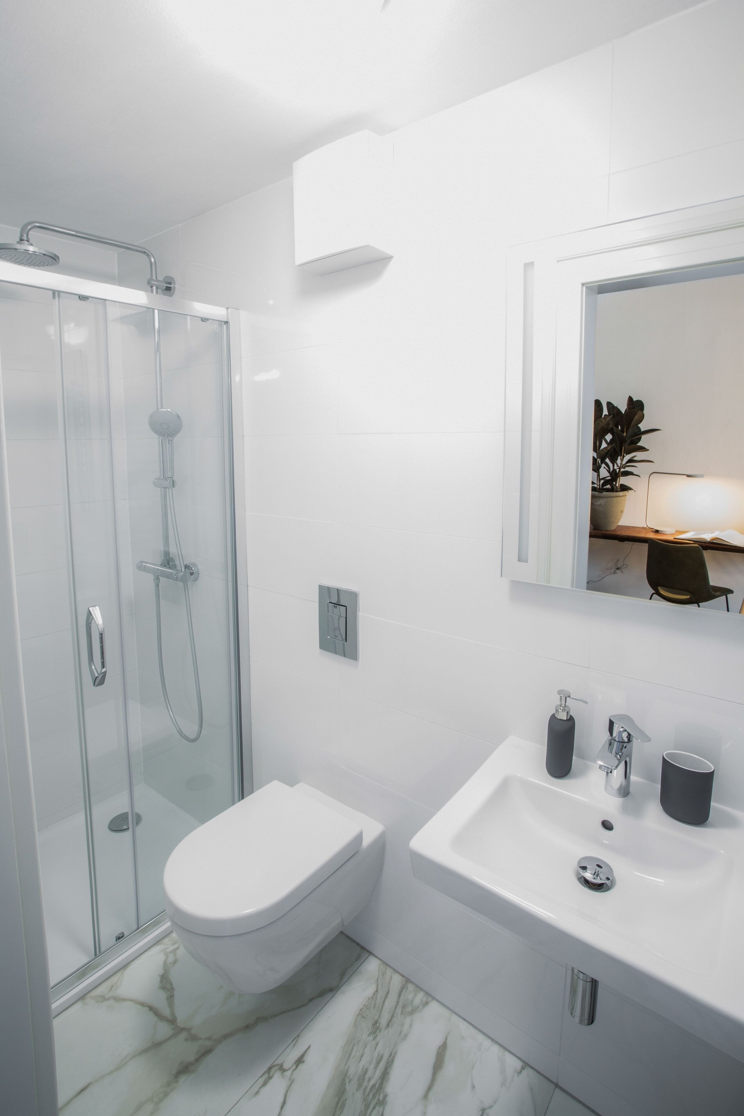 A modern bathroom with a glass shower enclosure, a white toilet, a sink with a mirror, and a marble floor.