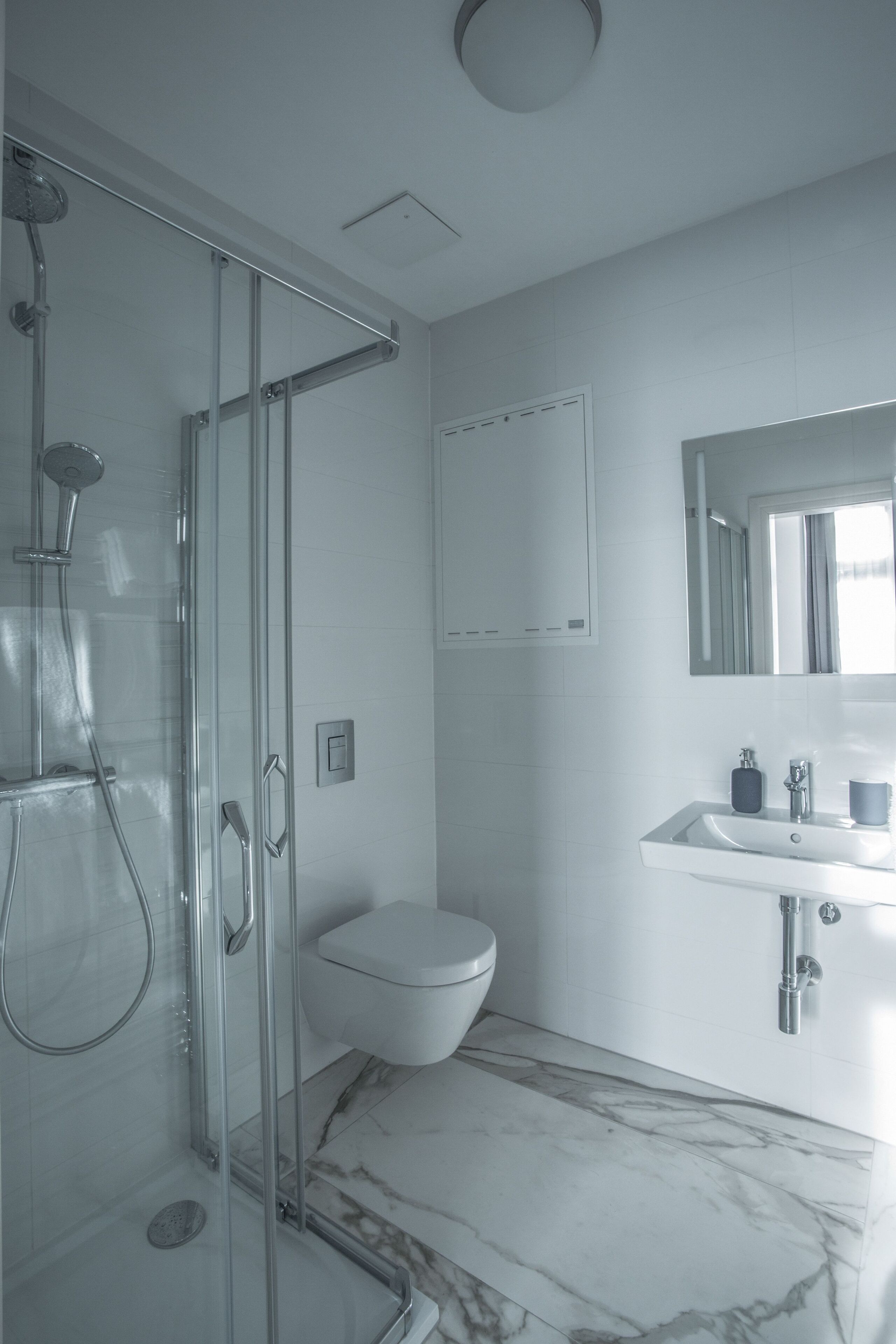 A modern bathroom with a glass-enclosed shower, a white toilet, and a marble-tiled floor.